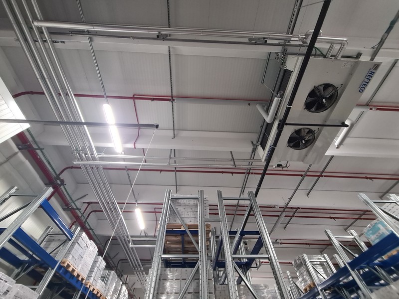 Unità Refteco a due ventilatori installata a soffitto sopra le scaffalature di un magazzino refrigerato